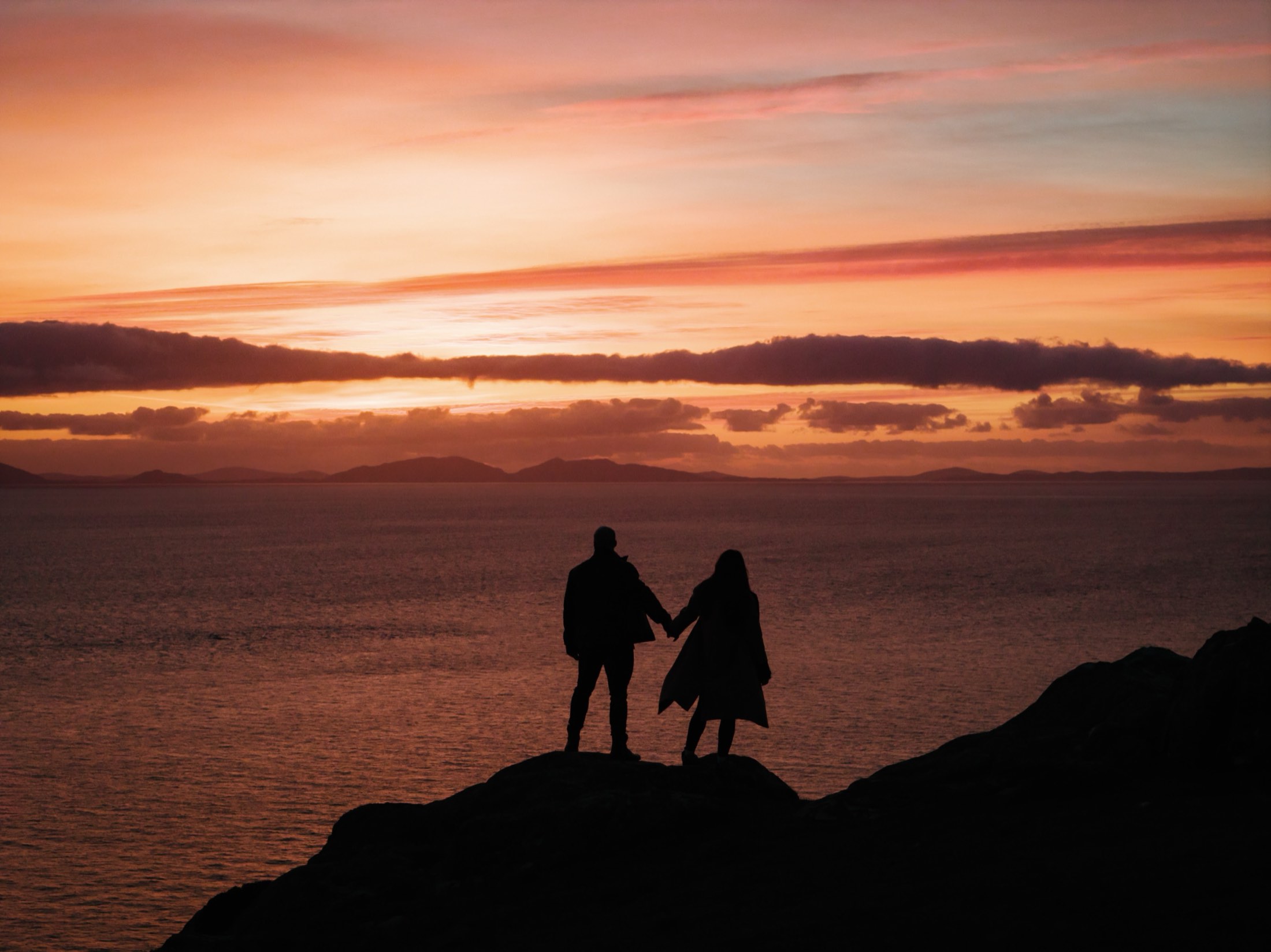 Danielle and Daniele hand in hand on the clifftop at sunset