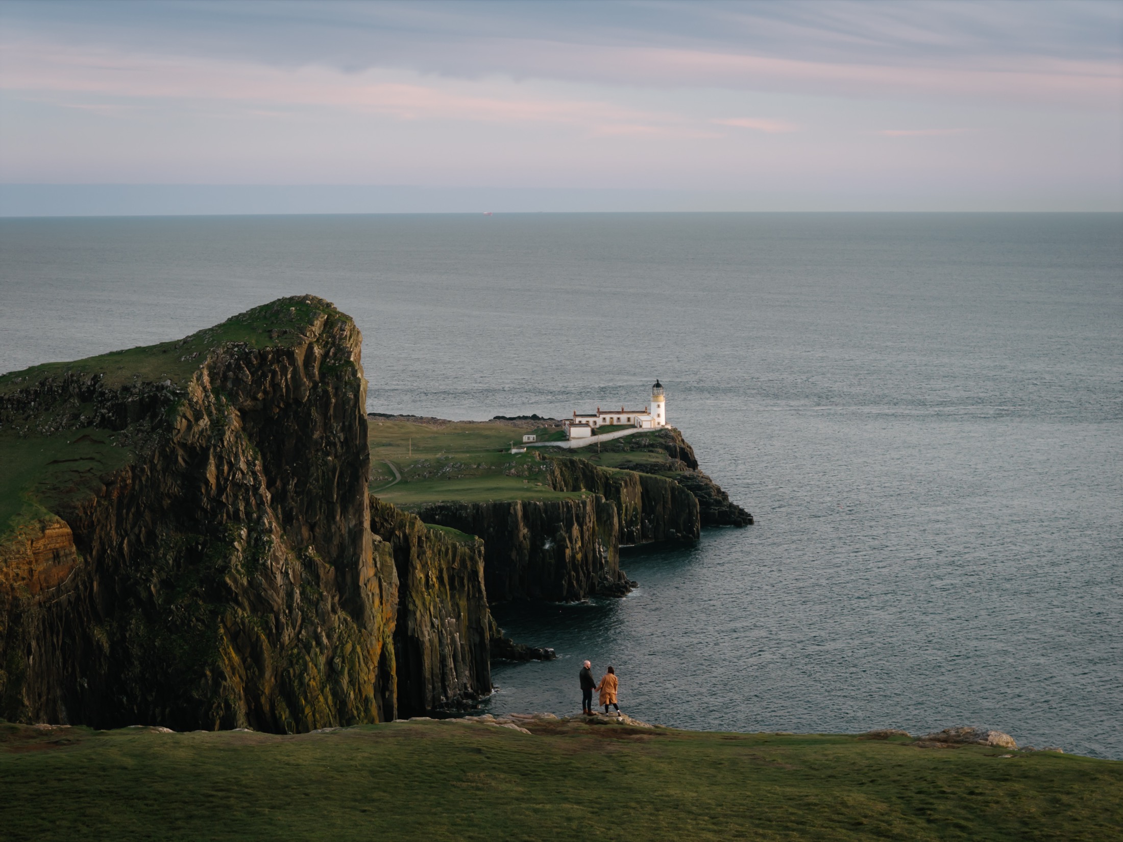 Daniele and Danielle small on the clifftop at Neist Point, the lighthouse beyond