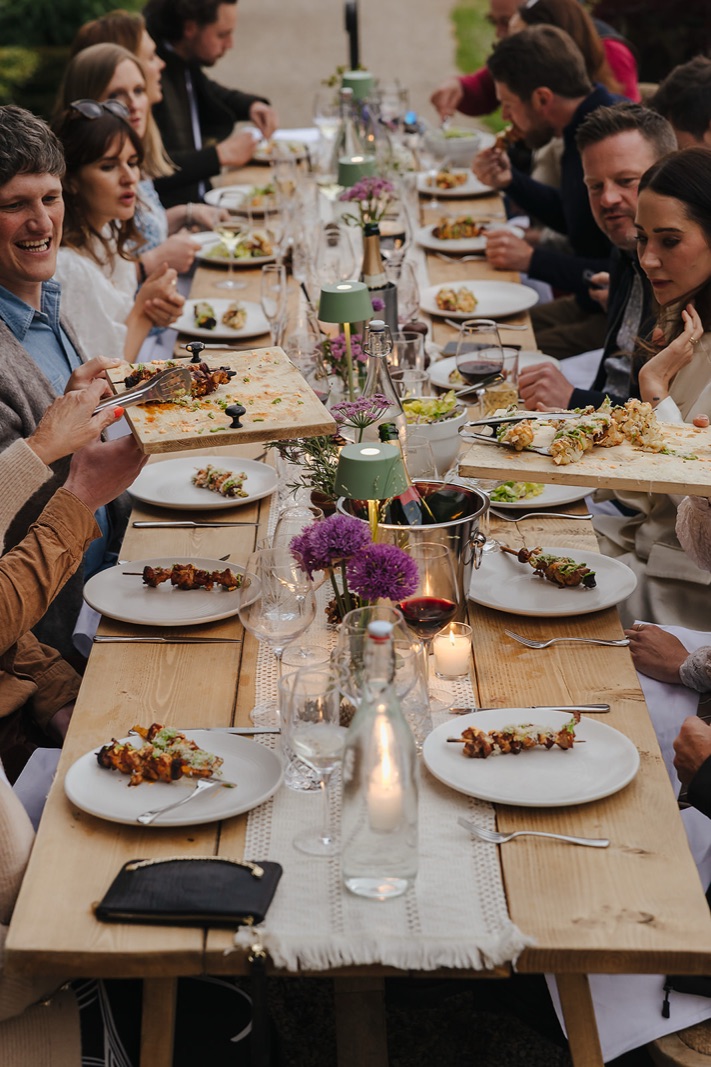 Guests eating and laughing down a long candlelit table