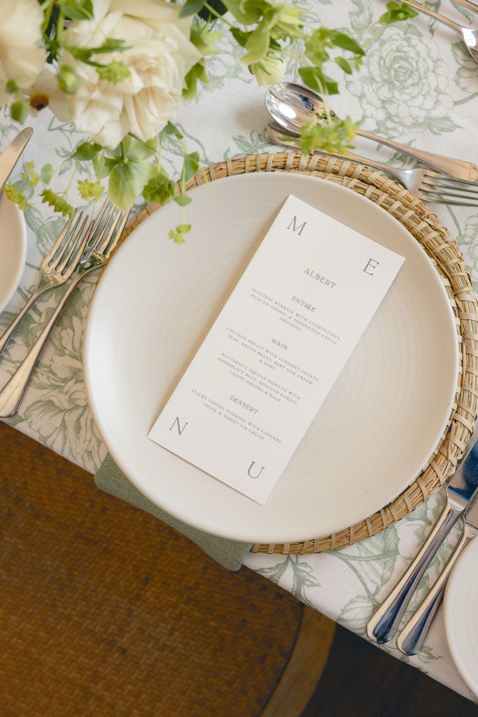 A place laid, menu card on the plate, white roses beside it